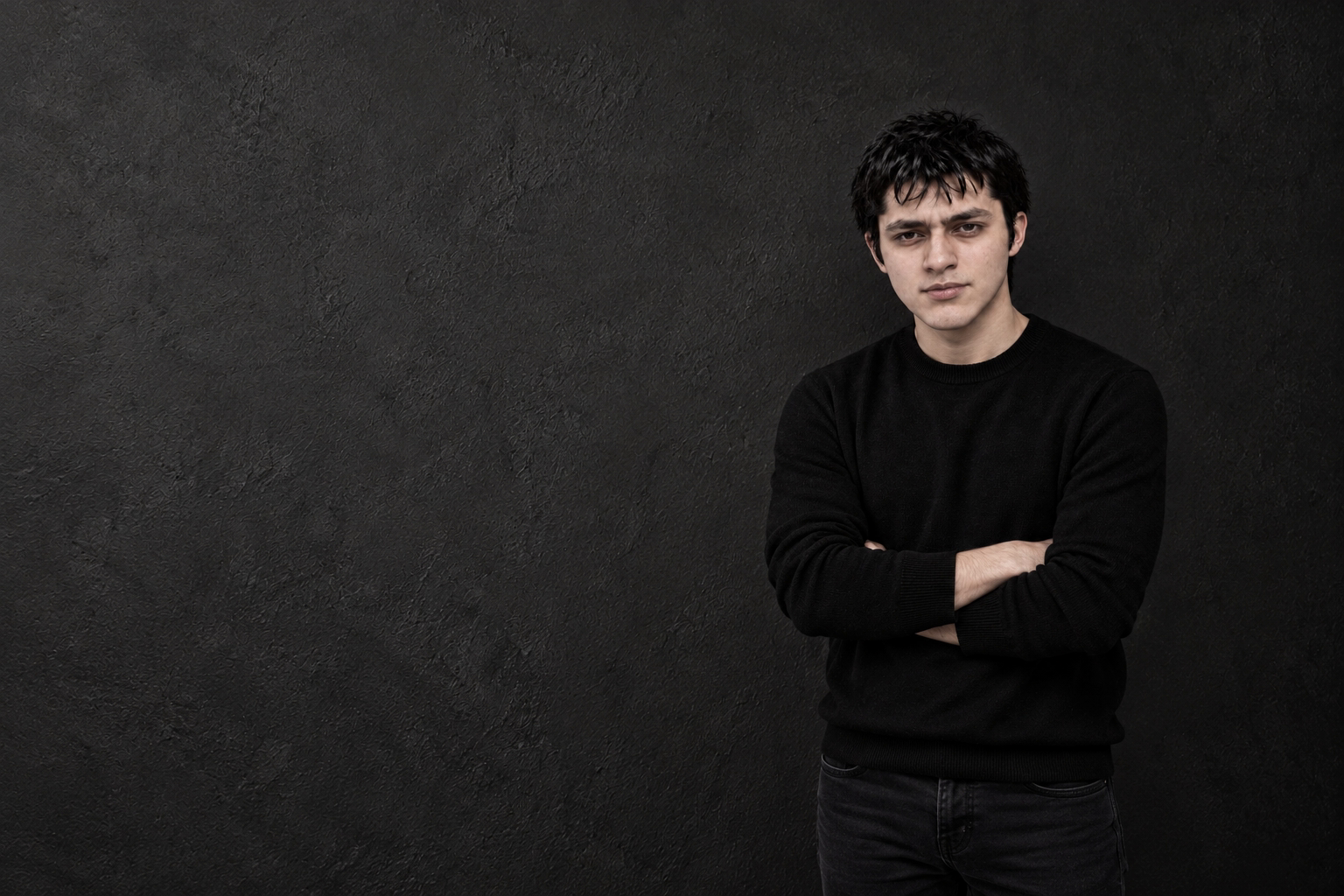 An edited monochrome portrait of Sam Sharma in a dark crewneck, standing with arms folded.